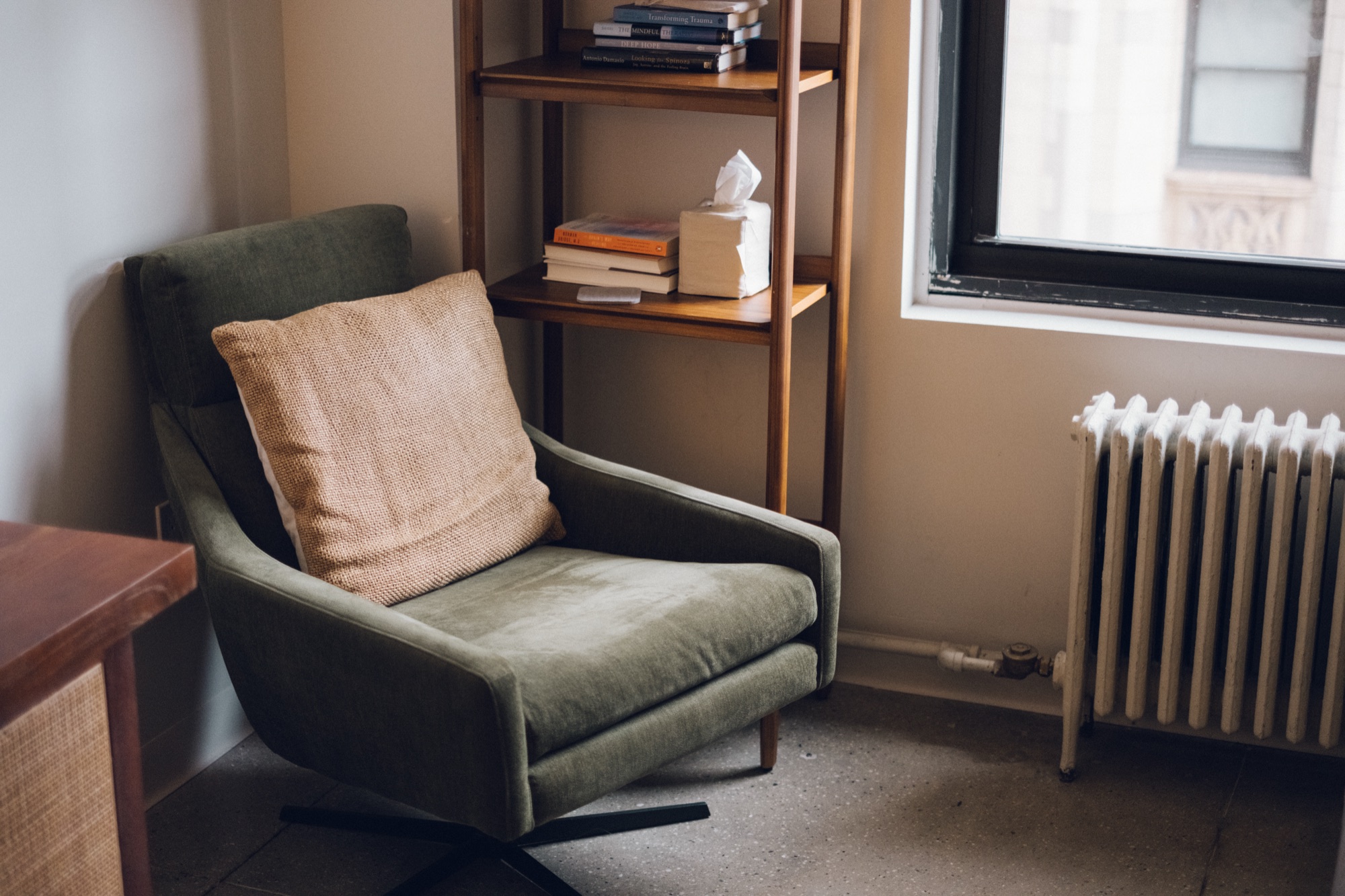 A green armchair beside a bookshelf and window in a therapy office.